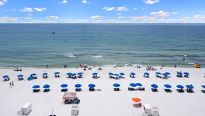 A beach with rows of blue umbrellas and lounge chairs, a clear sky, and the ocean in the background. - Beach Front Condo! Newly Renovated! Awesome views! Private Balcony! (Gulf Shores)