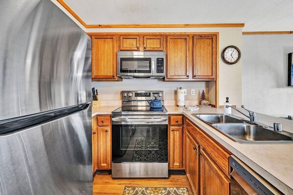 A kitchen with stainless steel appliances, wooden cabinets, a microwave, a stove, and a dishwasher.