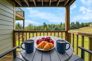 A wooden deck with a table set for breakfast, including croissants, strawberries, and grapes, and two coffee mugs. - 58 Powderidge, Snowshoe, WV - Cozy Chalet (Snowshoe)