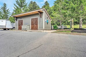 A small, single-story building with two large wooden doors, likely a garage or storage area, adjacent to a paved driveway.