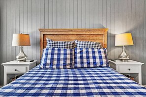 Ein Bett mit einer blau-weißen, karierten Tagesdecke, zwei passende Kissen, ein hölzernes Kopfende und zwei Nachttische mit Lampen.