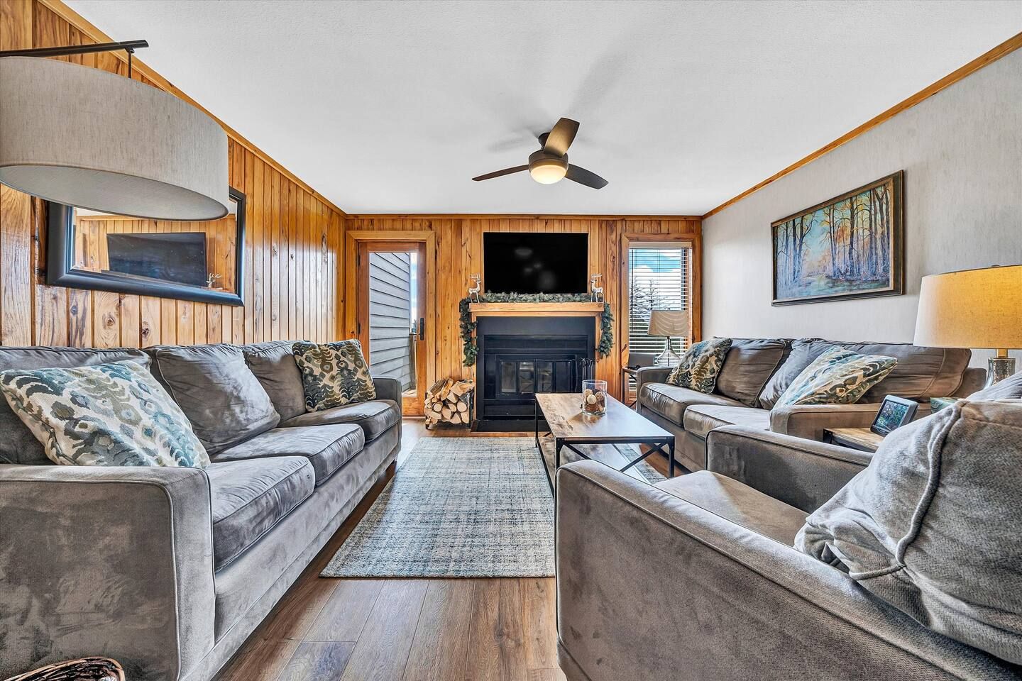 A cozy living room with a fireplace, two sofas, a coffee table, and a ceiling fan.