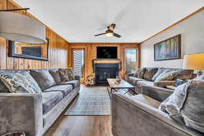 A cozy living room with a fireplace, two sofas, a coffee table, and a ceiling fan.