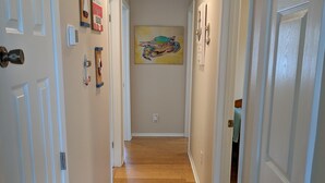 A hallway with wooden floors, white walls, and doors on both sides. There is a painting on the wall and a thermostat on the left wall.