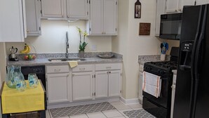 A kitchen with white cabinets, a black refrigerator, a microwave, and a stove. There is a yellow table with water bottles and a potted plant.
