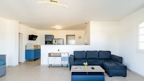 Una sala de estar moderna con un sofá azul oscuro, una mesa de centro y una cocina al fondo.