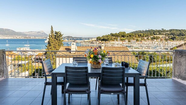 Una terraza con mesa y sillas, un jarrón de flores y vistas a un puerto deportivo y al paisaje urbano.