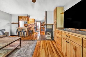 A modern kitchen with wooden cabinets, a dining area with bar stools, and a large flat-screen TV.