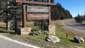 Placa para Ridgewood Mountain Crest com base de pedra e suportes de metal, rodeada por árvores e uma estrada sinuosa.