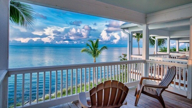 A covered outdoor area with a view of the ocean, wooden chairs, and a palm tree. - Indigo Reef Resort Villas and Marina (Marathon)