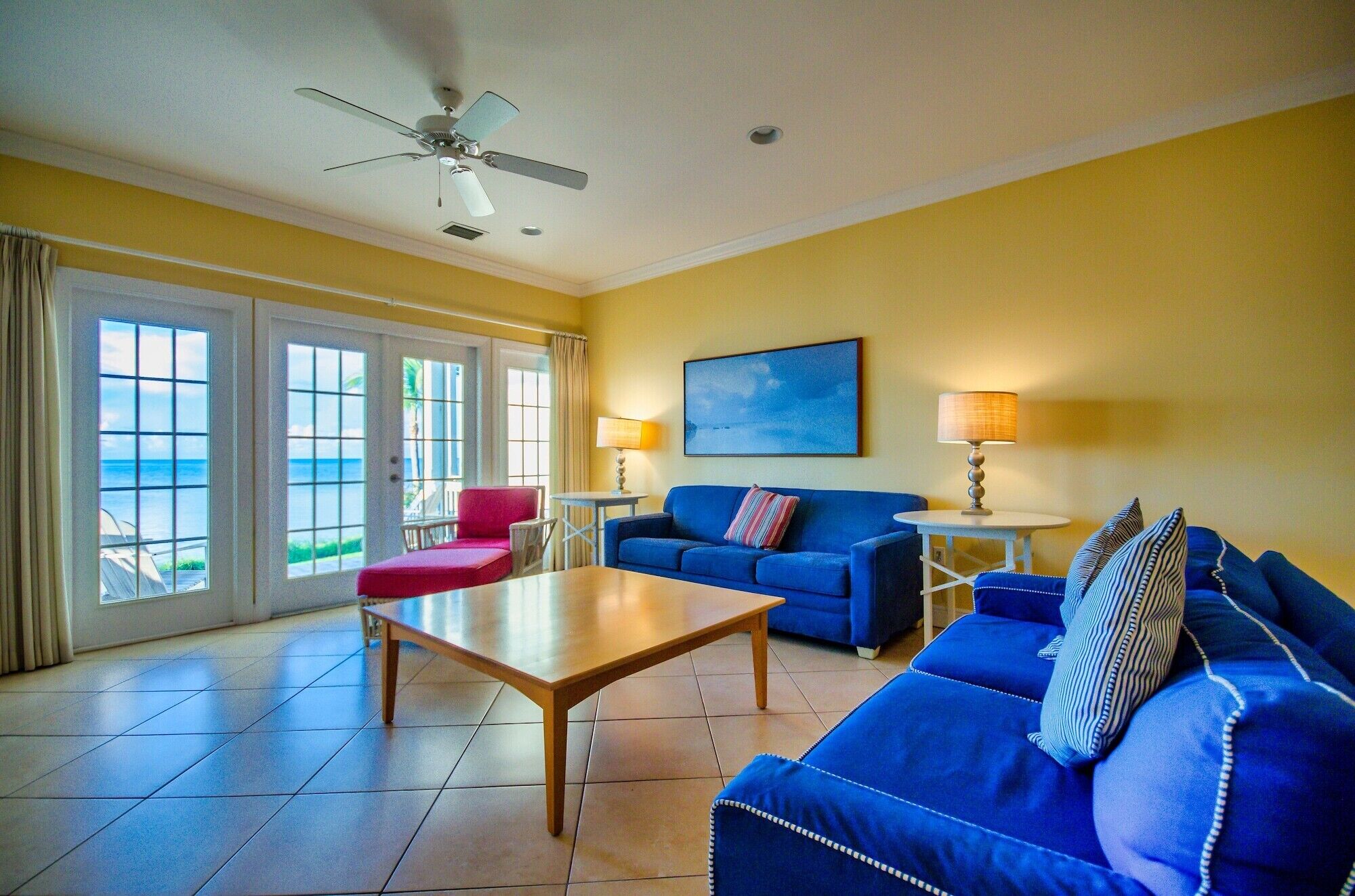 A room with a blue sofa, a red chair, a wooden table, and a ceiling fan.