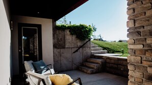 A modern outdoor seating area with a stone wall and a view of a grassy hill. - Modern Apt w/ Private Entry & Patio - Mtn Views (Smithfield)