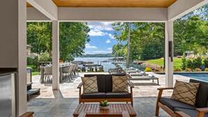 Une terrasse extérieure offrant une vue sur un lac, une piscine et un espace repas avec des tables et des chaises.