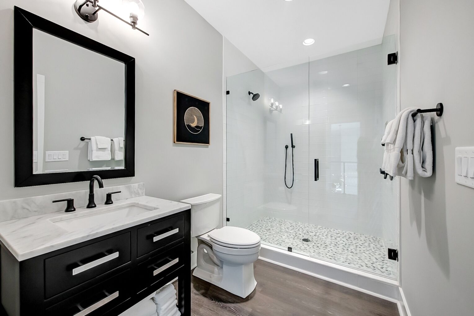 Un baño moderno con un espejo grande, un lavamanos blanco, un inodoro y una zona de ducha con paredes de vidrio.