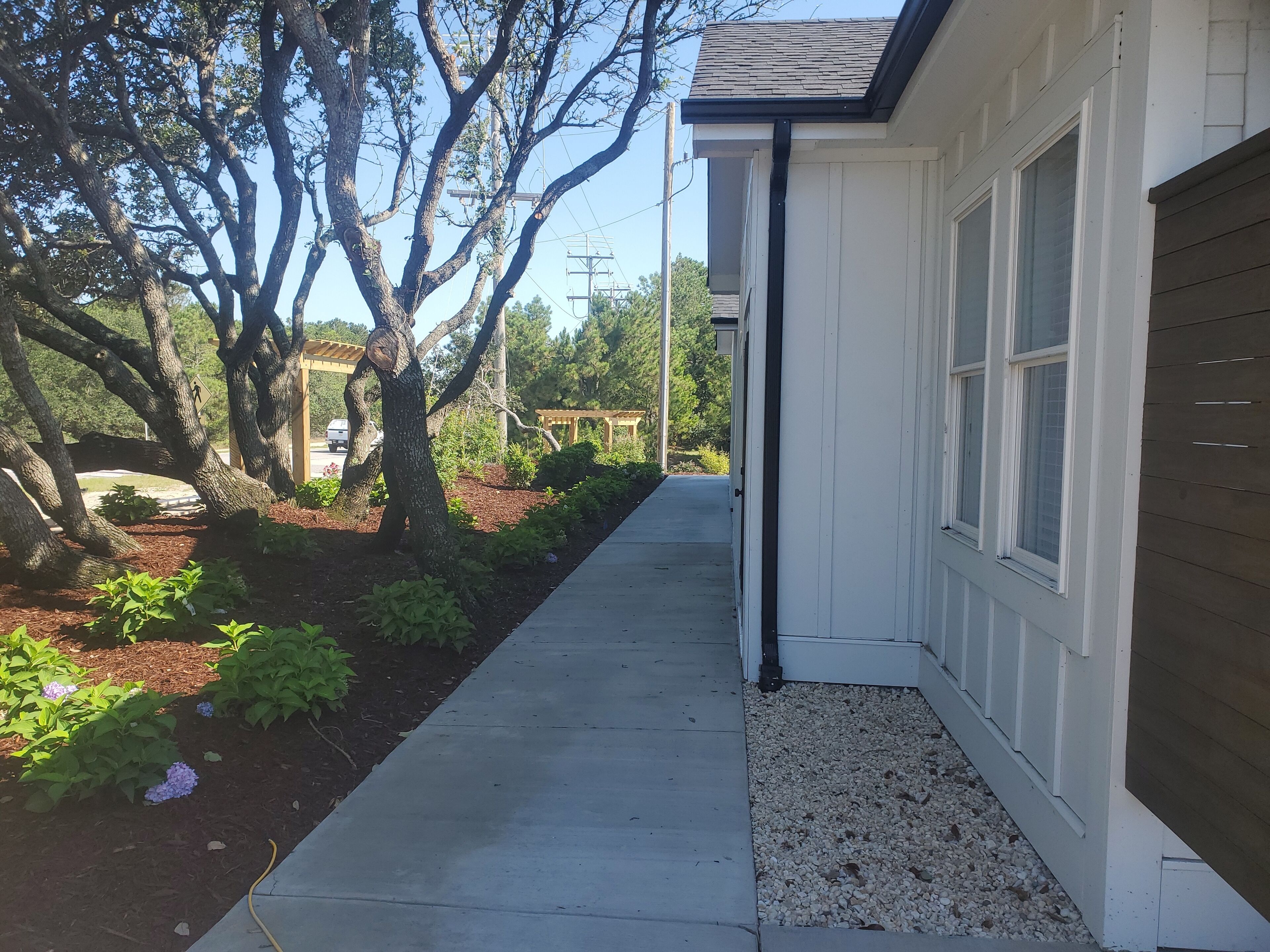 A pathway leading to a white building with a dark roof, surrounded by trees and shrubs.
