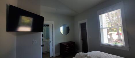 A bedroom with a bed, a ceiling fan, a TV, a mirror, and a window.