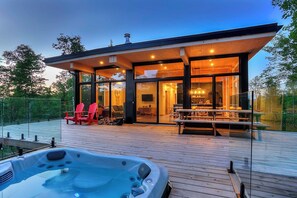 A modern house with a glass-enclosed patio, a hot tub, and outdoor seating.