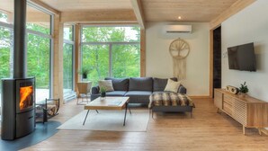 Un salon moderne avec un poêle à bois, de grandes fenêtres, un canapé, une table basse et un téléviseur fixé au mur.