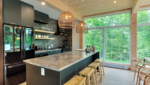 Une cuisine moderne dotée d’un grand îlot central, de meubles de rangement aux couleurs sombres et de tabourets en bois.