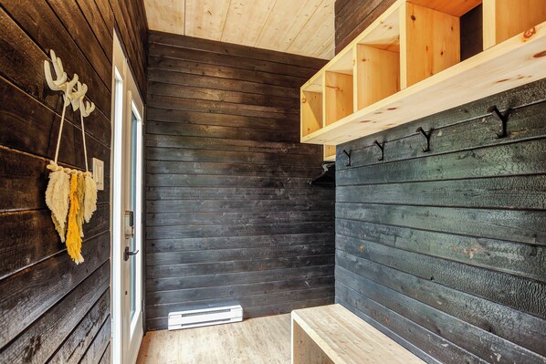 A wooden interior with a bench, a hanging decoration, and a shelf with hooks.