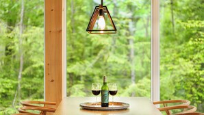 Une table à manger avec une bouteille et deux verres, le tout mis en valeur par un décor de forêt visible à travers de grandes fenêtres.