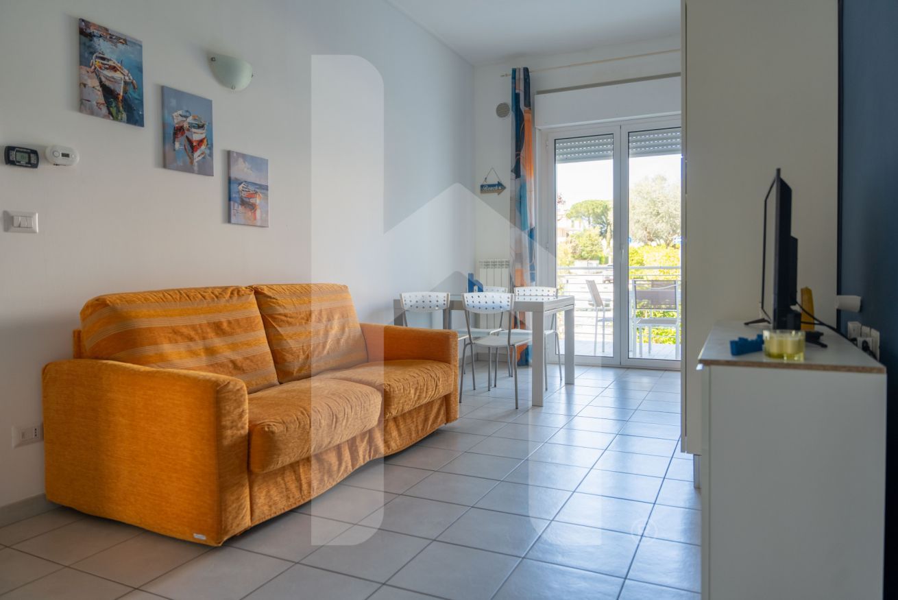 A modern living room with a sofa, a dining table with chairs, and a kitchen area with a fridge.