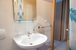Un baño con lavamanos blanco, un espejo y una puerta de ducha.