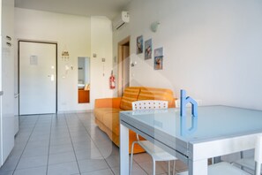 Una habitación moderna con una mesa de vidrio, un sofá con cojines naranjas, una puerta blanca y una pared decorada con cuadros.