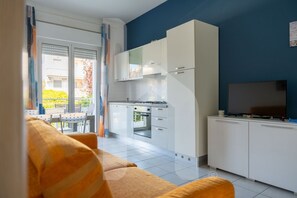 Una cocina moderna con armarios blancos, horno integrado y televisor de pantalla plana sobre un mueble.