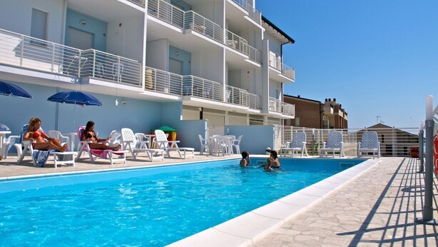 A swimming pool area with lounge chairs and umbrellas, a multi-story building with balconies, and a clear blue sky. - In an enchanting position, in a residential area just a stone's throw from the town center and directly on the territory of the Torre del Cerrano Marine Protected Area, the I Gabbiani residence offers you a relaxing vacation. Apartment two (Foggetta)