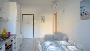 A modern kitchen with white cabinets, a dining area with a table set for four, and a gray sofa. - In an enchanting position, in a residential area just a stone's throw from the town center and directly on the territory of the Torre del Cerrano Marine Protected Area, the I Gabbiani residence offers you a relaxing vacation. Apartment two (Foggetta)