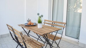 A wooden table with four chairs, a potted plant, and a plate with pastries on a balcony with a glass door and white walls. - In an enchanting position, in a residential area just a stone's throw from the town center and directly on the territory of the Torre del Cerrano Marine Protected Area, the I Gabbiani residence offers you a relaxing vacation. Apartment two (Foggetta)
