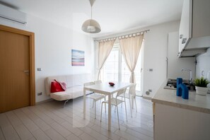 Une cuisine moderne avec des meubles blancs, un évier et une cuisinière. On y trouve une table à manger avec des chaises et une fenêtre avec des rideaux.