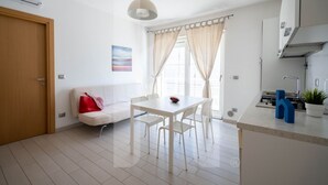 Een moderne keuken met witte kasten, een spoelbak en een fornuis. Er is een eettafel met stoelen en een raam met gordijnen.