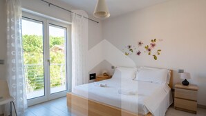 Een slaapkamer met een groot bed, een nachtkastje, een lamp en uitzicht op groen door een schuifdeur.