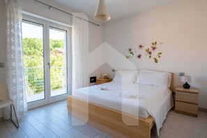 Une chambre avec un grand lit, une table de chevet, une lampe et une vue sur la verdure grâce à une porte coulissante.