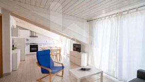 A modern living room with a blue chair, a white coffee table, and a grey sofa. There is a kitchen area with white cabinets and a stove in the background. - Mugo - Three-room apartment a few steps from the sea (Pineto)