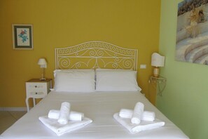 Quarto de hotel com cama, duas almofadas, mesa de cabeceira com abajur e um quadro na parede.