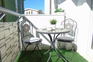 Um pequeno pátio exterior com uma mesa redonda e duas cadeiras, rodeado por um muro branco e uma vedação verde.