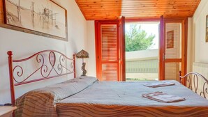 A bedroom with a bed, a nightstand, a lamp, a painting, and a window with shutters. - Pinetina Di Paolo - Second floor apartment, directly on the sea (Pineto)