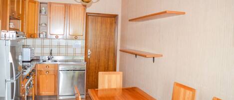 A compact kitchen with wooden cabinets, a stainless steel stove, and a dining table with chairs.