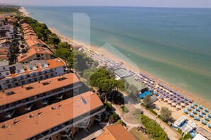 Ein Hotel an der Küste mit mehreren Balkonen, ein Strand mit Sonnenschirmen und freiem Blick auf das Meer.