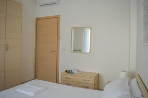 Een hotelkamer met een bed, een houten garderobe, een nachtkastje met spiegel en een wandairconditioner.