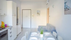 A modern kitchen with white cabinets, a dining area with a glass table, and a gray sofa. - I Gabbiani 10 - Ali - Two-room apartment on second floor with balcony (Foggetta)