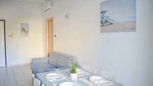 A dining area with a table set for four, a grey sofa, and a beach-themed painting on the wall. - I Gabbiani 10 - Ali - Two-room apartment on second floor with balcony (Foggetta)