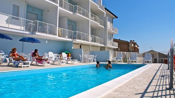A swimming pool with lounge chairs and umbrellas, a multi-story building with balconies, and a clear blue sky. - I Gabbiani 10 - Ali - Two-room apartment on second floor with balcony (Foggetta)