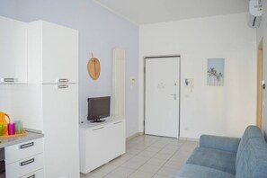 Een knus woongedeelte met een kitchenette, een televisie, een deur en een blauwe bank.