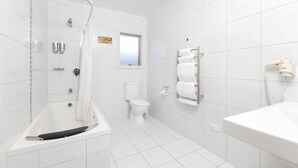A bathroom with a bathtub, toilet, and a towel rack. - Beach Street Motel Apartments (New Plymouth)