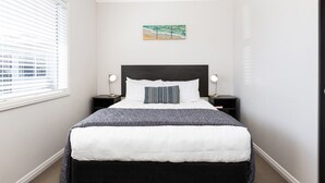 Un dormitorio con una cama, dos mesitas de noche, un velador, una ventana con persianas y un cuadro colgado en la pared.