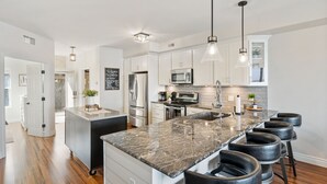 Una cocina moderna con armarios blancos, electrodomésticos de acero inoxidable, encimera de granito y taburetes negros.